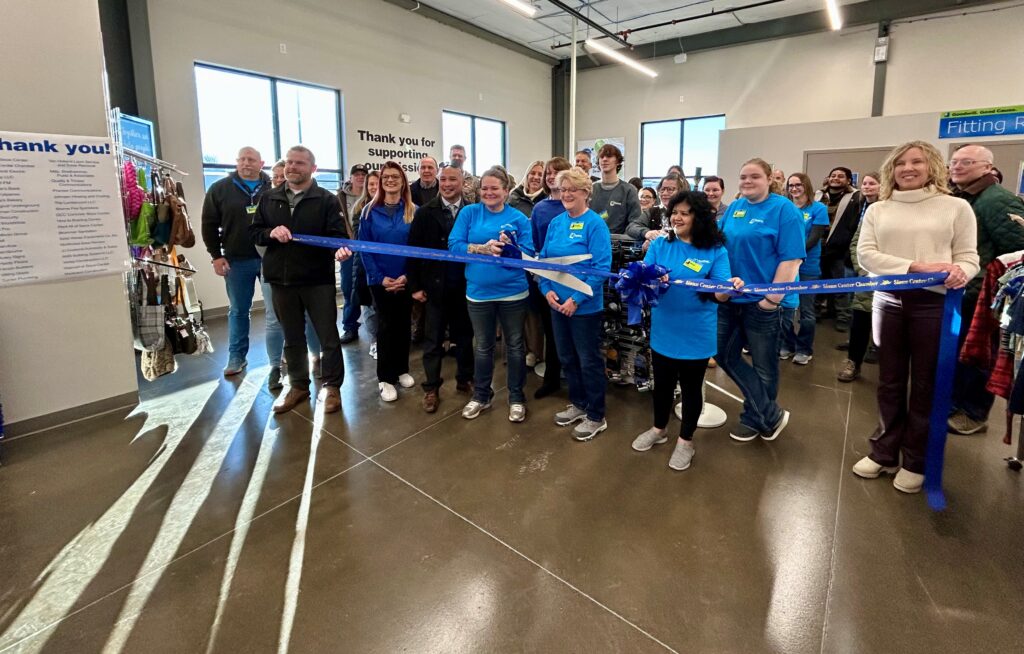 A group of people stand behind a blue ribbon while holding a giant pair of scissors, as they celebrate the opening of the new Goodwill of the Great Plains retail store in Sioux Center, Iowa on Thursday, Feb. 20th, 2025.